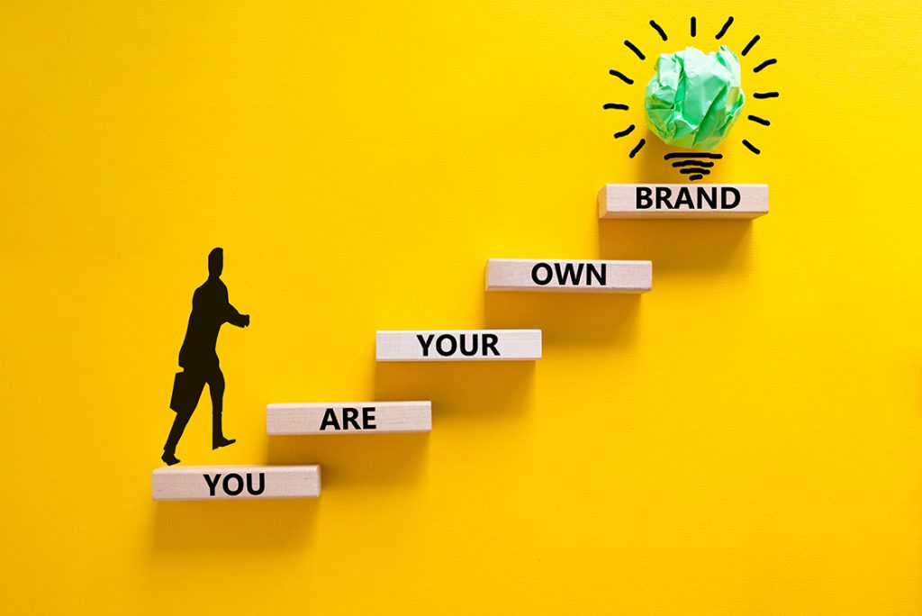 You are your own brand symbol. Wooden blocks with words You are your own brand. Beautiful yellow background, copy space. Businessman icon, light bulb. Business, you are your own brand concept.