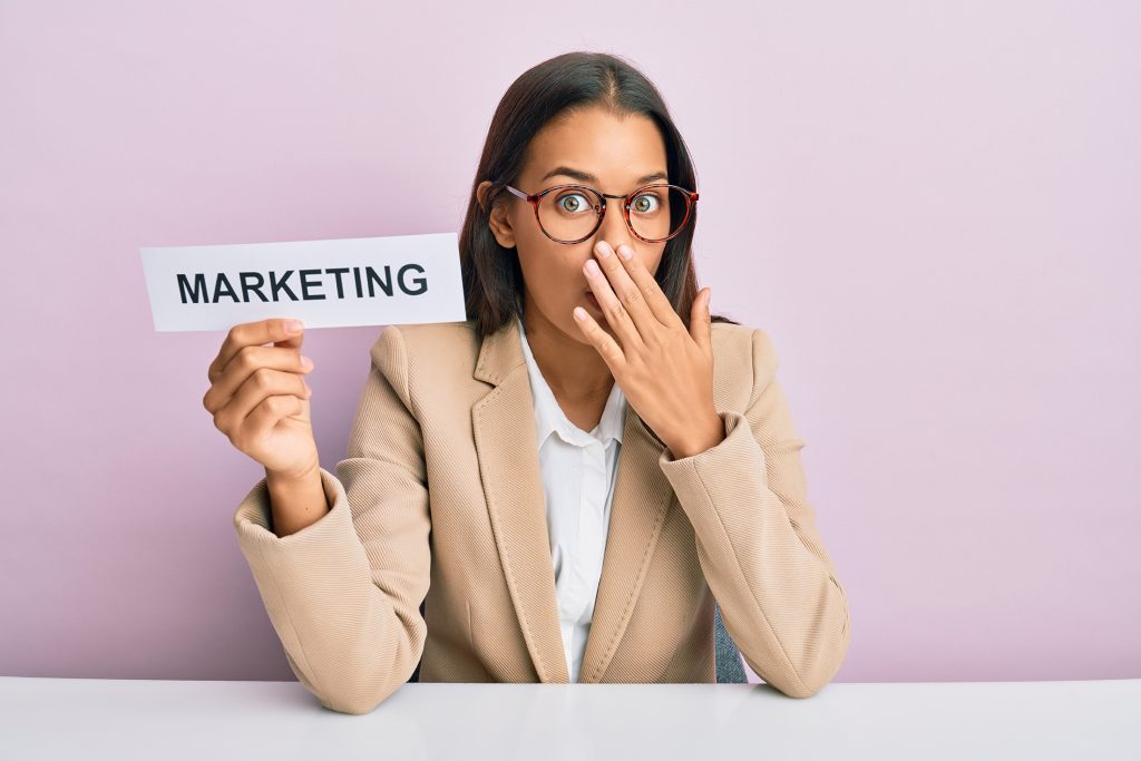 Beautiful hispanic business woman holding marketing message paper covering mouth with hand, shocked and afraid for mistake. surprised expression