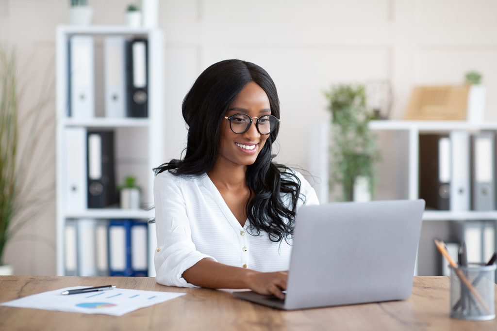 Beautuful black businesswoman working with laptop computer at desk in office. African American female entrepreneur typing document, checking email, participating in online meeting at workplace