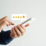 close up on customer man hand pressing on smartphone screen with gold five star rating feedback icon and press level excellent rank for giving best score point to review the service , business concept